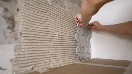 Mosaic tile kitchen apron. The hands of the master glue the mosaic tiles. Laying gray mosaic tiles by the hands of a master.