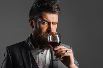 Winemaker smelling red wine in glass. Bearded sommelier tasting flavor and checking wine quality.