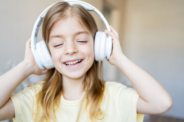 Close up portrait of happy cheerful little girl listening music in headphones .