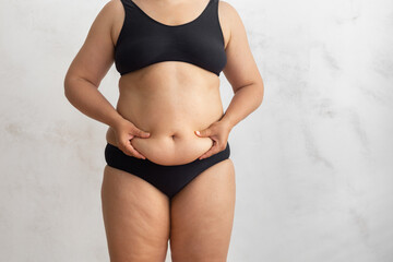 Unrecognizable overweight obese woman in black bikini touching and squeezing big dangling tummy. Hand self massage to friable cellulite skin. Food addiction, obsession, overeating problem. Health care