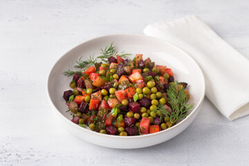 Vegetable salad vinaigrette with beets, potatoes, carrots, pickles, green peas and herbs in a white plate on a light blue background. Traditional Russian salad