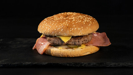 Delicious homemade hamburger, beef, bacon, cheese, on a black background