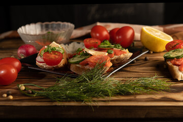 Sandwiches with red fish and vegetables lie on the plates. Dark wood background.