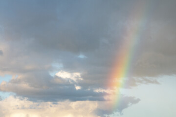 Fototapeta na wymiar A multi-colored rainbow spread across a cloudy blue sky.