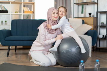 Middle age beautiful muslim sportswoman with her cute little daughter doing yoga exercise using...