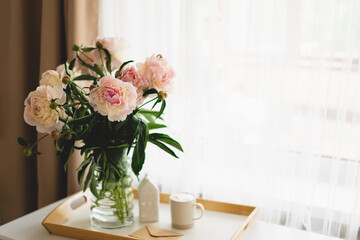 Still life details in home interior of living room. Open book with glasses, cup coffee and bouquet white pink peonies flowers. Read and rest. Cozy home