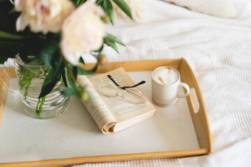 Still life details in home interior of living room. Open book with glasses, cup coffee and bouquet white pink peonies flowers. Read and rest. Cozy home