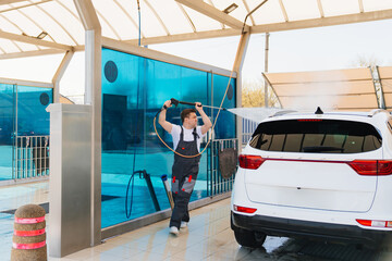 self-service car wash. a man in a work jumpsuit washes the car from a hose. 