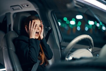  frightened woman is sitting behind the wheel of a car in a black shirt, wearing a seat belt, expressing her emotions, holding her hands near her face from fright. Photo on the topic of road safety