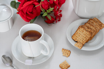 cup with tea on a table, cookies on a plate, bouquet of red roses