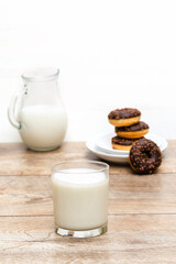 Mini donuts covered with chocolate glaze served with bottle, jug, glass of milk. Stack of tasty sweet sugar creamy or icing doughnuts dessert food on plate and napkin on kitchen. national donuts day