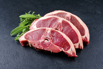 Raw lamb saddle back chop steak with herbs offered as close-up on a black design board with copy...
