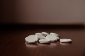 pills on a wooden table. A group of medical round white natural pills lies on a wooden dark brown...