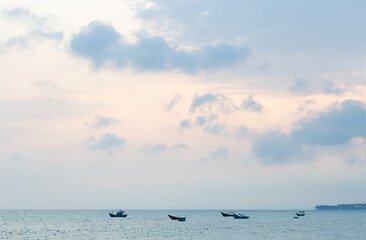 Pink and blue sunset on the coast of the South China Sea. Silhouettes of fishing boats near the horizon. Vietnam.