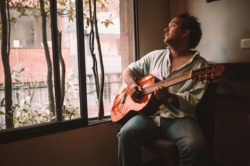 man playing guitar in front of window