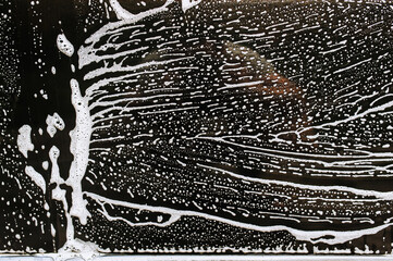 Background, texture of the black surface of a metal car door in white soapy foam after washing.