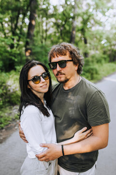 Beautiful, stylish bearded man and hippie brunette woman in sunglasses hugging and smiling outdoors in the park. Portrait, photograph of people in love.