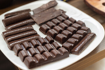 Close up of various dark chocolate bars on a white plate. Wooden table
