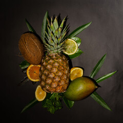 Attractive arrangement of fresh tropical fruits - pineapple, mango, coconut, orange slice and lemon on a black background