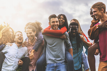 Group of young friends of different races and cultures have carefree fun playing piggyback together outdoors - youth culture lifestyle concept