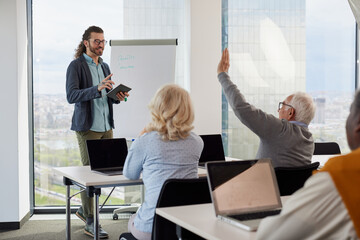 A young teacher is explaining senior students how to solve an informatics problem on tablet while one of them asking questions.