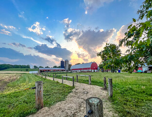 A gravel cow lane with a dairy barn and two silos and storm clouds at sunset in the summer. © Margaret Burlingham