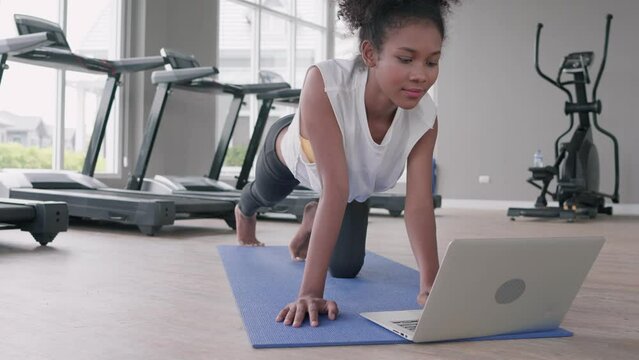 Fitness young black woman doing exercise yoga in gym. African american female loook at laptop computer lesson practicing Yaga plank pose on social online internet class. Healthy lifestyle concept.