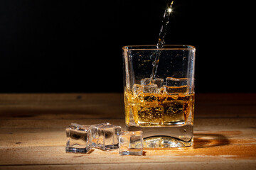 Pouring whiskey into a glass with ice cubes on a black background