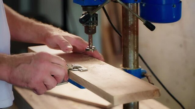 joiner is installing furniture loop in wooden detail, working in his workshop, closeup of hands