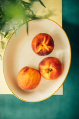 three peaches in bowl next to vase of Tarragon herb