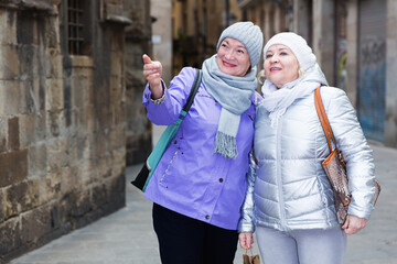 Two smiling senior ladies on vacation roaming around foreign city