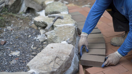 Closeup of putting brick pavers in place along an edge of a rock wall.