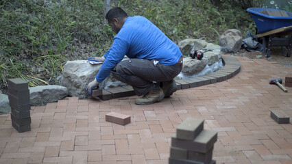 Man with ear protection putting brick pavers in place along an edge of a rock wall.