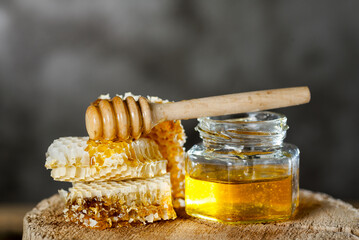 honeycomb and Fresh transparent honey in a glass jar with dipper on cut of a tree