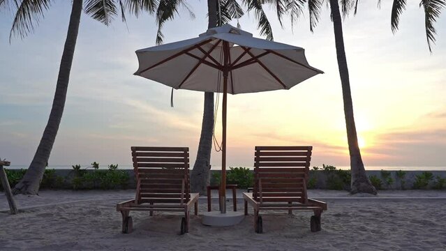 Close-up of two empty sun longers under a shade umbrella on the beach facing out toward the setting sun.