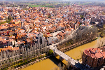 Picturesque aerial view of Spanish city of Aranda de Duero with terracotta tiled roofs of residential buildings on banks of river in spring - obrazy, fototapety, plakaty