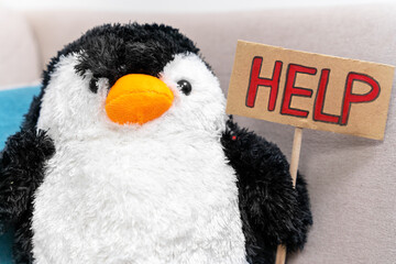 Cute stuffed toy in the shape of penguin with handmade sign with inscription HELP, front view. Call...