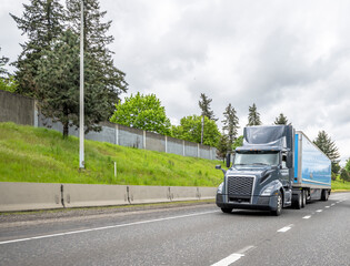 Gray stylish big rig semi truck transporting cargo in dry van semi trailer moving on the multiline...