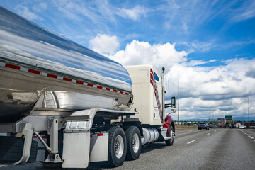 Light beige classic big rig semi truck transporting liquid cargo in tank semi trailer driving on the wide highway road