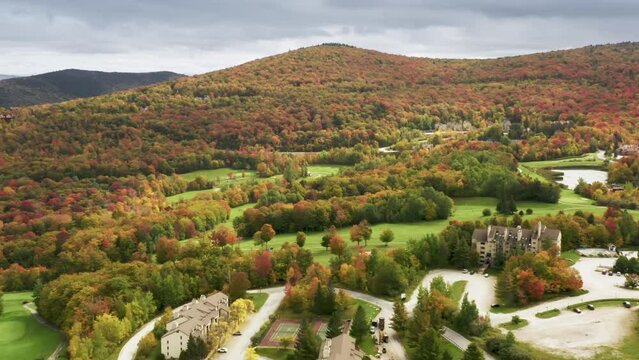 Killington mountain resort with colorful red orange fall foliage forest landscape background on sunny autumn day. Cinematic 4K aerial ski resort with hotels and golf course on sunny vibrant fall day
