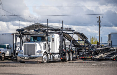 White car hauler big rig semi truck with empty modular semi trailer standing on the industrial...