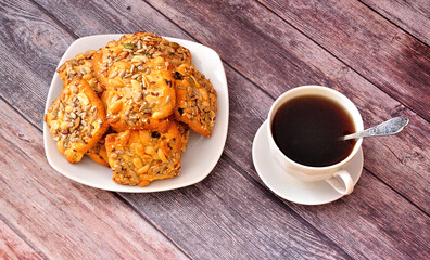 A stack of shortbread cookies with sesame and peanuts on a plate and a cup of tea.