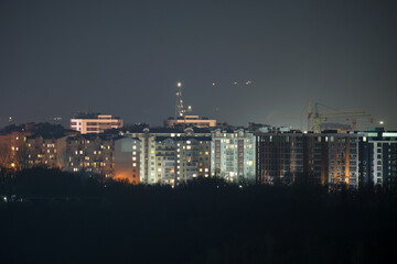 Dark silhouette of tower cranes at high residential apartment buildings construction site at night. Real estate development