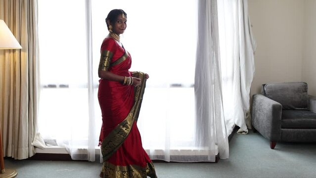 Indian woman wearing red orange traditional royal saree and jewellery showing turning smile bright window backlight