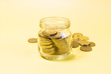 Yellow coins in a glass jar on the background of a scattering of yellow coins.