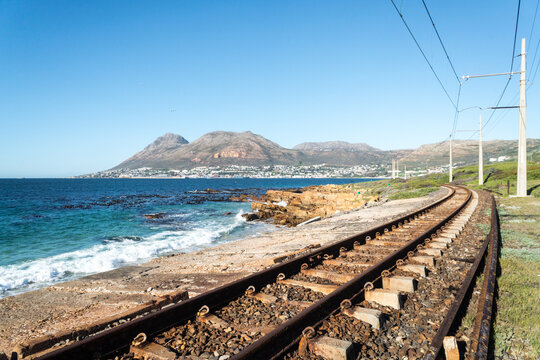 railway on the coast, adjacent to the sea or ocean with Simon's town in the distance in Cape Town, South Africa
