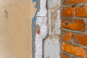 Dismantling the facade covering of a private house. Expanded polystyrene insulation on a wall of aerated concrete block against the background of a wall of red ceramic bricks
