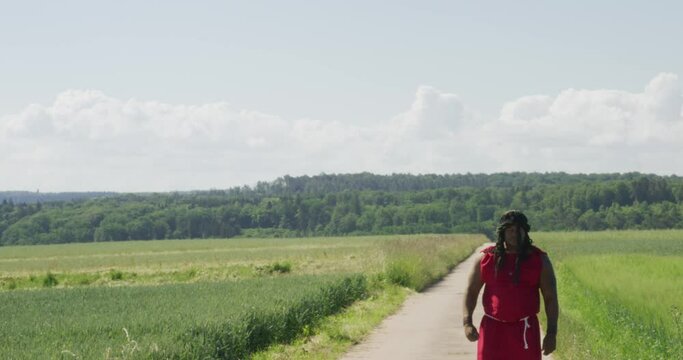 Samson walking close pass screen from mid distance along old road in green pastures, Biblical character with long dreads, Israelite warrior and judge, black male in old testament, Christian