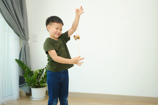 Cute little Asian school boy child having fun learning how to play with a yo-yo toy alone in living room at home, Photo in real life interior