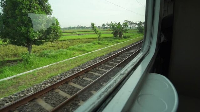 Ride the train sitting by the window looking at the view of the tracks and rice fields outside the window the train is speeding towards its destination